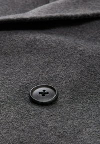 Grijze viltstof met een glanzende ronde zwarte knop met vier gaten, die een zachte textuur en een gladde afwerking toont.