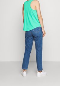 Top verde senza maniche, vestibilità ampia, abbinato a jeans blu a gamba dritta. Sneakers bianche completano l'outfit, visto da dietro.