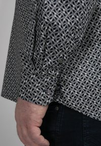 Langærmet shirt met een marineblauw en wit geometrisch patroon, voorzien van geknoopte manchetten en een structuurelement in de stof.