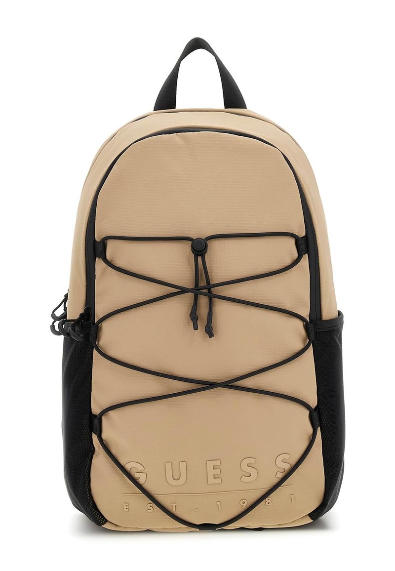 Beige tygryggsäck med svarta accenter, utrustad med en elastisk snodddesign, framträdande logotyp och ett handtag på toppen för bärande.