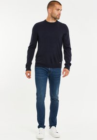 Námořnický svetr s kulatým výstřihem, ribbované manžety a lem, v kombinaci s modrými džíny a bílými teniskami. Jednoduchý, přiléhavý design, bez viditelných vzorů.