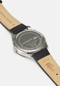 Montre avec bracelet en cuir noir, boîtier en acier inoxydable, cadran rond, logo gravé au dos et étanche jusqu'à 5 bars.