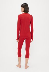 Top ajustado de manga longa vermelha e leggins capri feitas de material elástico. Textura suave com um design simples, sem padrões visíveis ou peças metálicas.