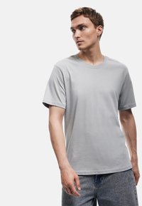 Camiseta de cuello redondo en gris claro, hecha de un tejido suave, con mangas cortas y un corte relajado, combinada con unos vaqueros de denim en azul claro.