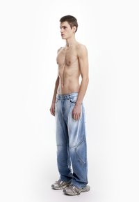 Svijetloplavi traper oversized traperice s jedinstvenim dizajnom panela, izblijedjelom teksturom i opuštenim krojem, uparene sa srebrnim tenisicama.