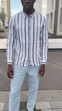 Wit overhemd met grijze strepen, gecombineerd met lichtblauwe jeans. De stof lijkt lichtgewicht, met een klassieke kraag en lange mouwen.