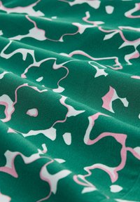 Tela verde con un patrón floral en rosa y blanco. La textura es suave con un ligero brillo, y el diseño tiene un toque abstracto.