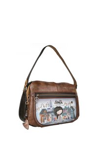Bolso de hombro de cuero marrón con un bolsillo frontal con cremallera que presenta una ilustración colorida de edificios y personajes. Incluye un charm en forma de corazón.
