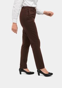 Bruine op maat gemaakte broek met een gladde textuur, elastische tailleband en plooien aan de voorkant, gecombineerd met zwarte hakken en een wit overhemd met lange mouwen.