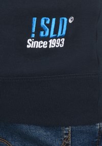 Navy sweatshirt featuring blue and white embroidered text reading “!SLD Since 1993,” with ribbed cuffs and a textured fabric.