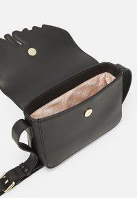 Černá kožená kabelka s unikátním klopou ve tvaru obličeje, zlatým zapínáním na cvok a béžovou podšívkou s vzorem. Součástí je nastavitelný ramenní popruh.