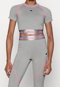 Šedý krátký sportovní top s růžovými akcenty a logem; ve spojení s legínami s vysokým pasem s růžovými bočními švy a páskem s logem.