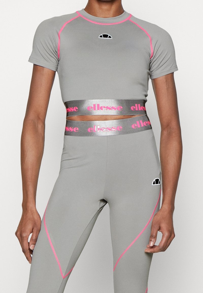 Šedý krátký sportovní top s růžovými akcenty a logem; ve spojení s legínami s vysokým pasem s růžovými bočními švy a páskem s logem.