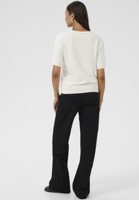 Haut blanc à manches courtes avec un col rond, assorti à un pantalon noir évasé. Texture lisse ; design minimaliste ; pas de motifs ni d'accents visibles.