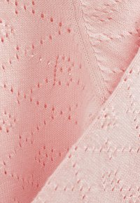 Ljust rosa stickad tyg med en strukturerad mönster. Har små hål och en subtil glans, som visar på mjukt, delikat hantverk.