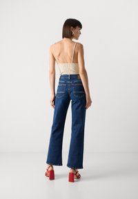 Top ribbed beige chiaro con spalline sottili, abbinato a jeans a vita alta blu scuro con gamba larga e sandali con tacco blocco rossi.