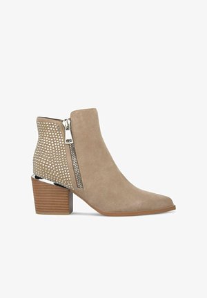 Bottes en matériau suédine beige, à bout pointu, avec fermeture éclair sur le côté et clous décoratifs métalliques à l'arrière, dotées d'un talon empilé.