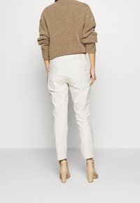 Vita avslappnade byxor med sidofickor, kombinerade med en brun texturerad tröja. Modellen bär ljusa klackskor.