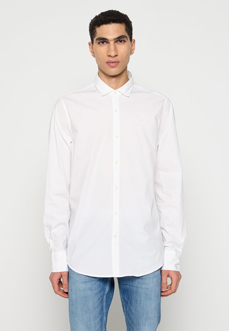 Weißes Langarmhemd aus Baumwolle mit Button-Down-Kragen, das eine dezente Textur hat und einen geraden Saum aufweist, kombiniert mit blauen Jeans.