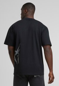 Black cotton t-shirt with short sleeves, relaxed fit, and a large gray graphic on the back. Smooth texture and simple design.