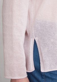 Hellrosa, leichtgewichtiger Pullover mit langen Ärmeln, der seitliche Schlitze und einen strukturierten Stoff aufweist. Der Saum hat ein kontrastierendes Stichdetail.