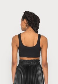 Top corto nero con spalline larghe e una texture morbida, abbinato a una gonna plissettata nera con una vita elastica.