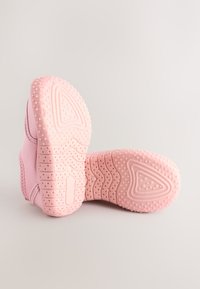 Paire de chaussures de bébé roses et douces avec semelles texturées antidérapantes exposées sur une surface claire.
