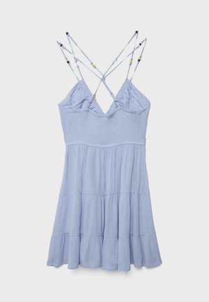 Hellblaues ärmelloses Sommerkleid mit mehrstufigem Rock und überkreuzten, mit Perlen besetzten Spaghettiträgern vor einem einfarbigen Hintergrund.