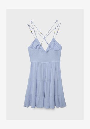 Hellblaues ärmelloses Sommerkleid mit mehrstufigem Rock und überkreuzten, mit Perlen besetzten Spaghettiträgern vor einem einfarbigen Hintergrund.