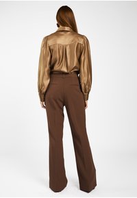 Glanzende, bronzen blouse met puffmouwen en een kraag, gecombineerd met een bruine, op maat gemaakte broek met brede pijpen en zakken.