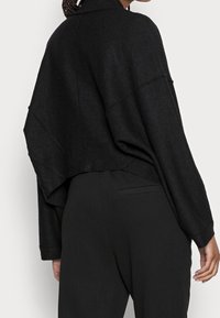 Czarna krótka kurtka wykonana z teksturowanej tkaniny, z szerokimi rękawami i asymetrycznym dołem. W połączeniu z czarnymi spodniami.