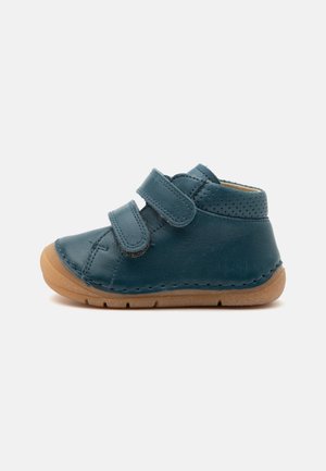 Chaussure en cuir bleu marine pour tout-petit avec deux brides velcro réglables et semelle en caoutchouc marron clair, présentée de profil sur fond blanc.