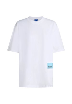 T-shirt blanc uni à manches courtes avec col rond et une petite étiquette rectangulaire bleu clair près de l'ourlet inférieur à l'avant côté droit.