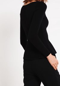Zwarte lange mouw top met een aangesloten ontwerp, geribbelde textuur en een peplumrand. Minimalistische stijl die soepele lijnen en rondingen benadrukt.