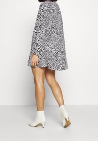 Šaty s černobílými skvrnami a dlouhými rukávy, s rozšířeným lemem, doplněné krémovými kotníkovými botami a hladkou texturou.