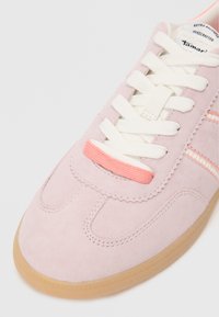 Helle rosa Wildledersneaker mit weißen Schnüren, ausgestattet mit einem strukturierten pinken Akzent und einer Gummisohle. Retro-Design mit dezenten Nähten.