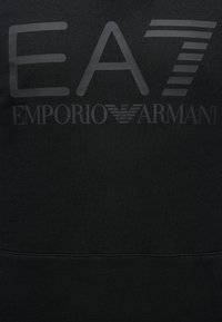 Svart genser med en fremtredende grå logo med teksten "EA7" og "EMPORIO ARMANI". Glatt tekstur med et rent design og subtile detaljer.