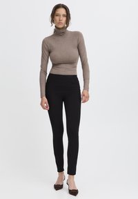 Černé kalhoty s vysokým pasem a slim fit, spárované s těsným taupe rolákem. Hladká tkanina s jemnou texturou. Jednoduchý design.