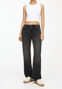 Jeans neri a gamba dritta con vita a media altezza, caratterizzati da un classico design a cinque tasche e un leggero sbiadimento. Abbinati a un top corto bianco.