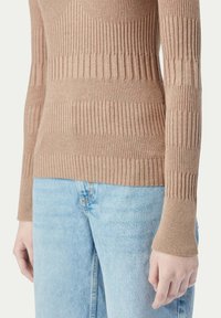 Brun ribbad stickad topp med långa ärmar, med varierande ribbmönster och en figurnära design; matchad med ljusblå jeans.