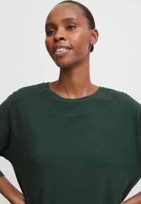 Donkergroen, T-shirt met korte mouwen gemaakt van zachte stof; heeft een ronde halslijn en een losse pasvorm voor comfort. Glad oppervlak zonder patronen.