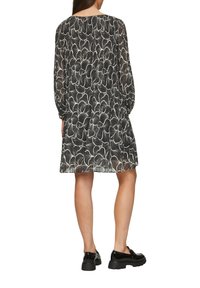 Robe noire avec un motif floral blanc, coupe ample, manches longues et encolure arrondie. Portée avec des chaussures noires à semelle épaisse.