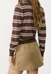 Brązowy sweter w paski z prążkowanym dołem i mankietami, zestawiony z beżową zamszową spódnicą, charakteryzującą się gładką fakturą i dopasowanym krojem.