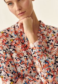 Langærmet blomstret bluse med et multicolor print bestående af pink, røde, blå og hvide blomster på en marineblå baggrund; knappet manchet detalje.