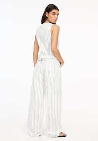 Witte gestreepte mouwloze top en brede broek combinatie. De stof heeft een gladde textuur met blauwe verticale strepen en gestikte accenten.