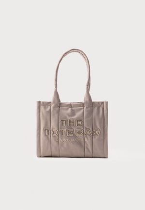 Pehmeä taupenvärinen suorakaiteen muotoinen tote-laukku, jossa on pehmustetut pystysuorat paneelit, kaksinkertaiset pyöristetyt kahvat ja etupuolella kohokuvioitu teksti "THE TOTE BAG MARC JACOBS".