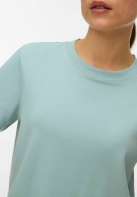 Lichtblauwe trui met ronde hals, gemaakt van zachte stof, met korte mouwen en een gladde textuur, met minimale ontwerpdetails.