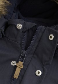 Marineblaue Jacke mit Reißverschluss und Lederzug, Druckknöpfen sowie einem weichen, strukturierten Innenfutter und einer mit Fell gefütterten Kapuze.