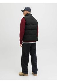Chaleco de plumas negro sobre un suéter de punto rojo, combinado con pantalones marineros y zapatos beige. El chaleco presenta un cuello alto y una textura suave.