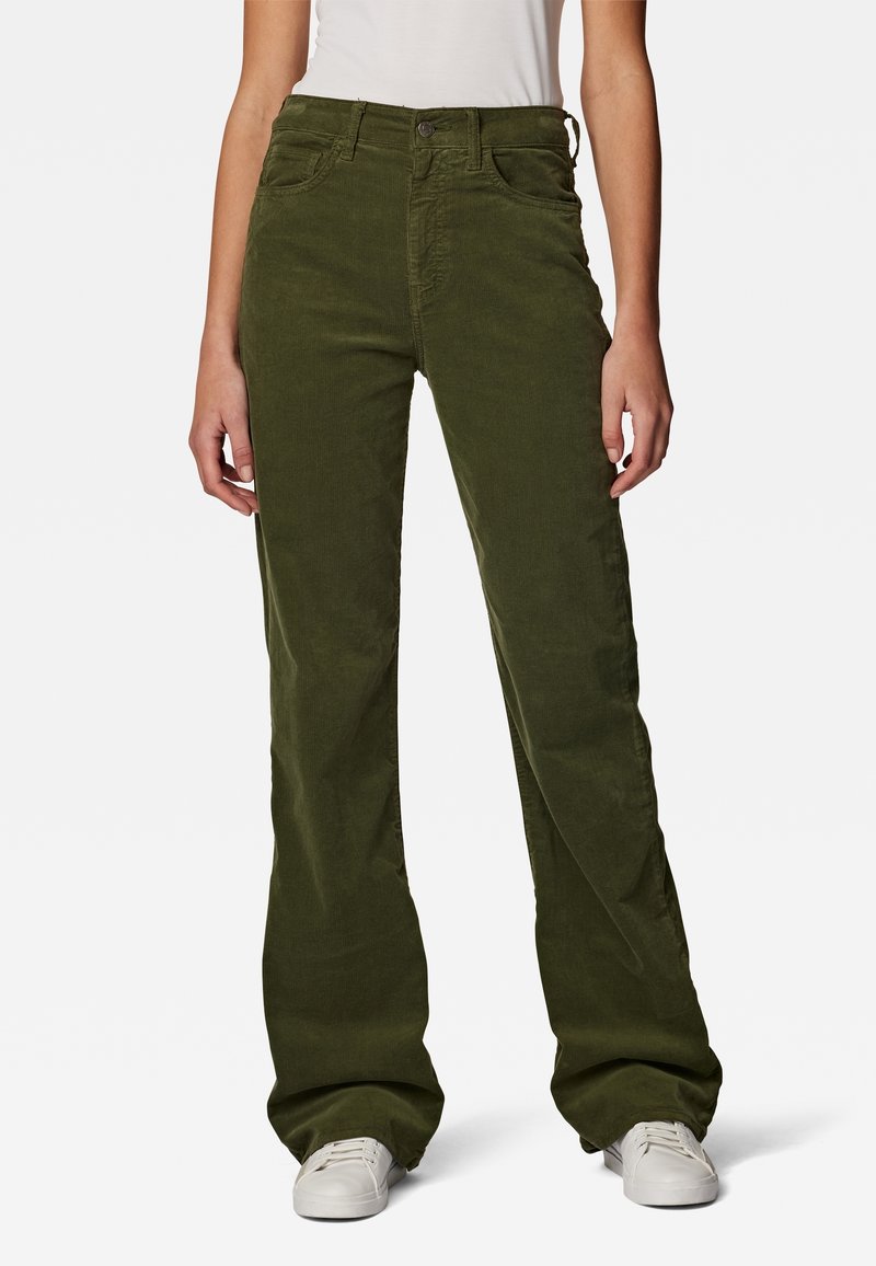 Personne portant un pantalon large en velours côtelé vert olive avec fermeture par bouton et zip, associé à des baskets basses blanches.